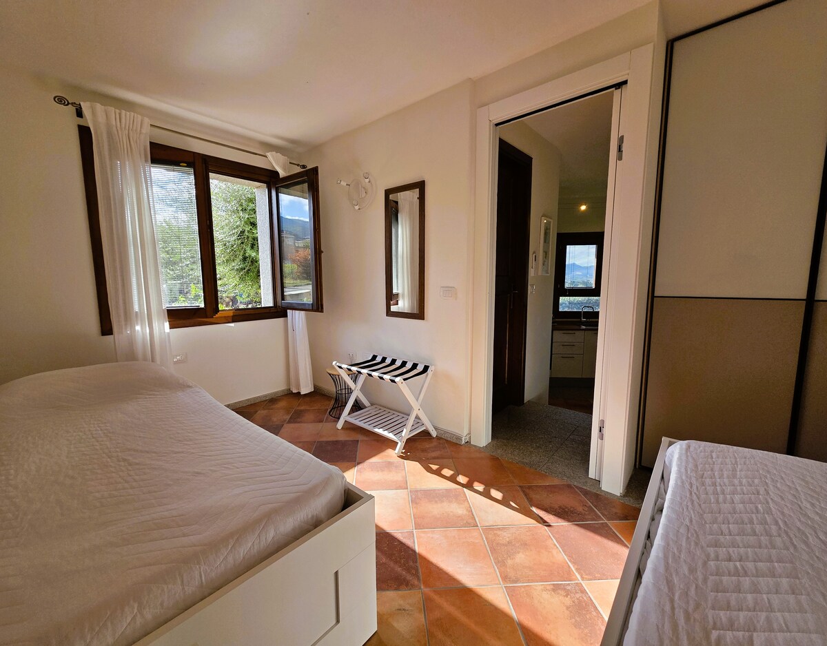 Helles und gemütliches Zimmer mit zwei Einzelbetten und Möbeln mit einfachem und funktionalem Design. Das große Fenster bietet einen schönen Blick auf den umliegenden Garten und gibt viel natürliches Licht in die Umgebung. 