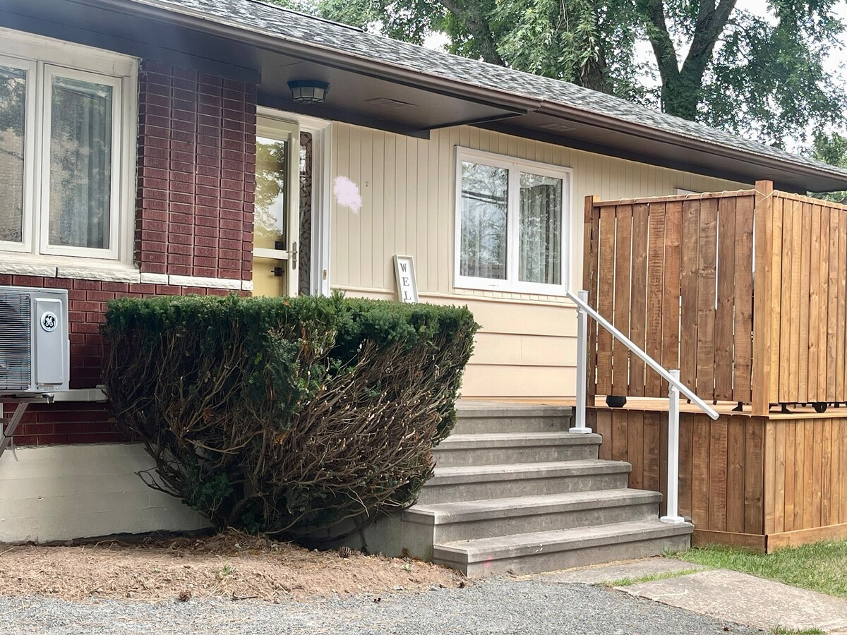 The exterior of the home features a set of concrete steps leading to a welcoming doorway. A well-maintained hedge and wooden fence provide privacy. Large windows allow for natural light, and an air conditioning unit is visible on the side wall.