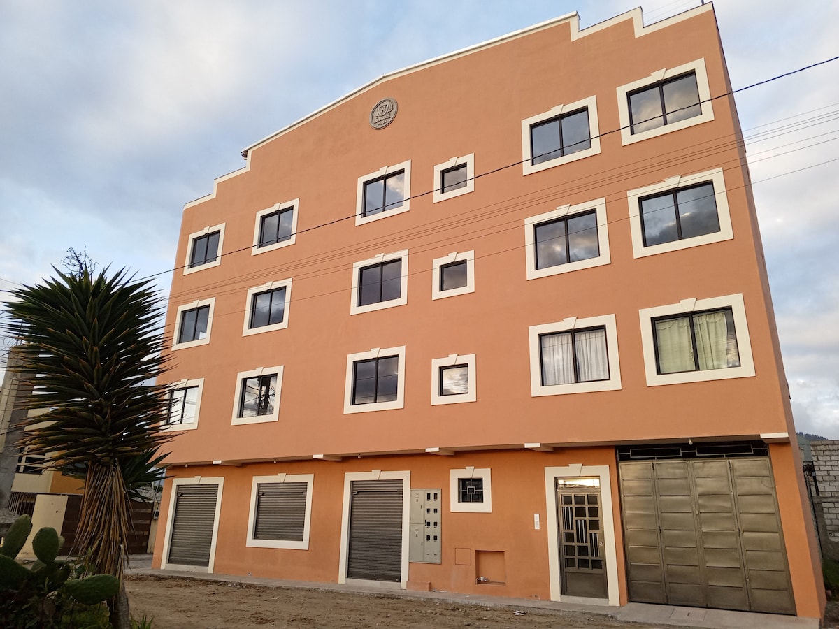 A multi-story building with a distinct curved top features a warm peach exterior. Large windows characterize the façade, allowing natural light to permeate the interior. A prominent entrance is centrally located, with shuttered storefronts visible below.