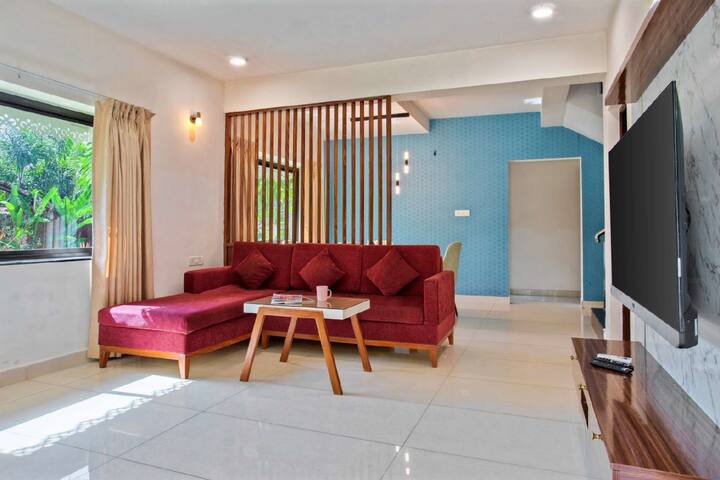 The villa’s living room is a sunlit oasis, featuring plush sofas and a large flat-screen TV for entertainment. Chandeliers shimmer like stars, and an elegant fireplace invites warmth, complemented by stunning views.