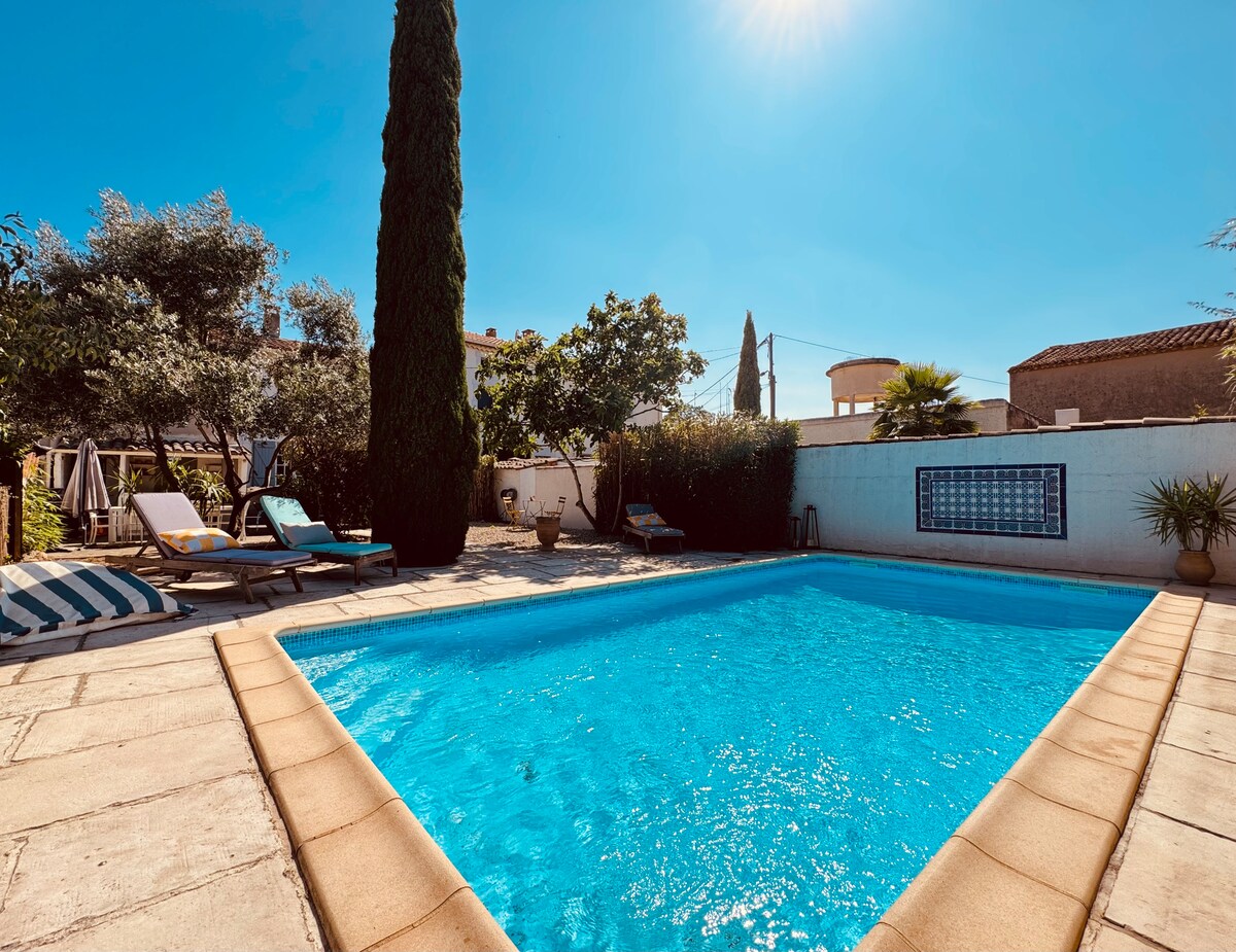 A refreshing pool is surrounded by sun loungers and lush greenery. The clear blue water reflects the sunlight, creating a calming atmosphere. Tall cypress trees provide shade, enhancing the outdoor space for relaxation and leisure.