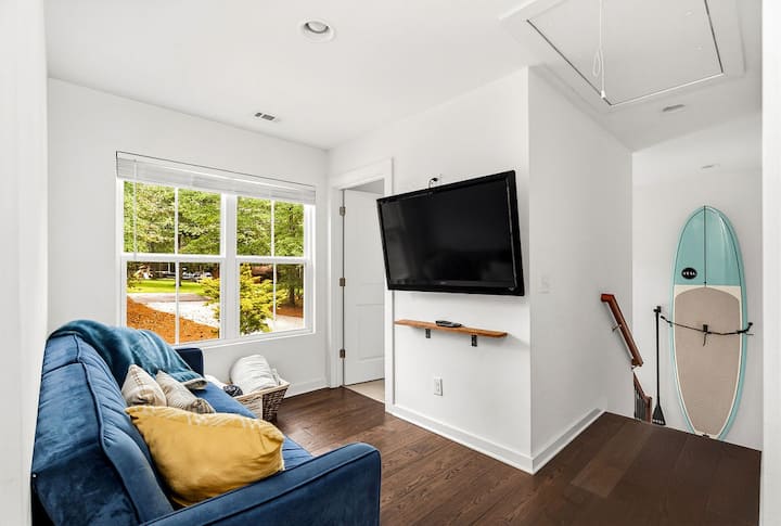 Bright coastal lounge with large windows, comfy sofa, and wall-mounted TV