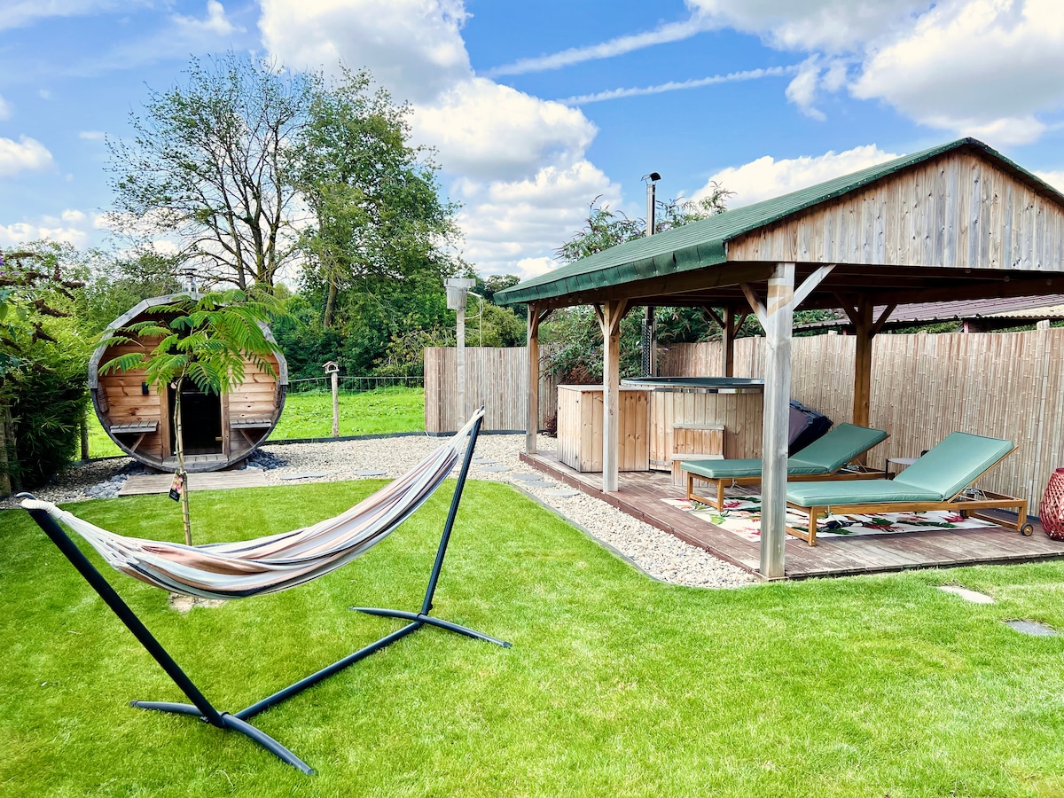 A private outdoor relaxation area is featured, with a hammock gently swaying beside well-maintained green grass. To one side, a wooden structure houses a sauna, while a hot tub is positioned nearby, accompanied by lounge chairs and a decorative rug.