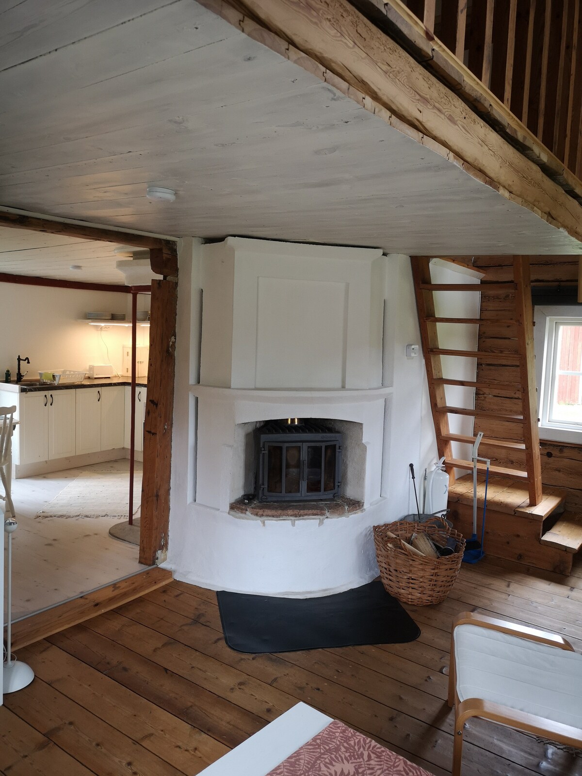 A central fireplace is featured in the open living area, providing a cozy focal point. Wooden floors complement the rustic interior, while a staircase leads to the upper level. Natural light enters through nearby windows, highlighting the inviting atmosphere.