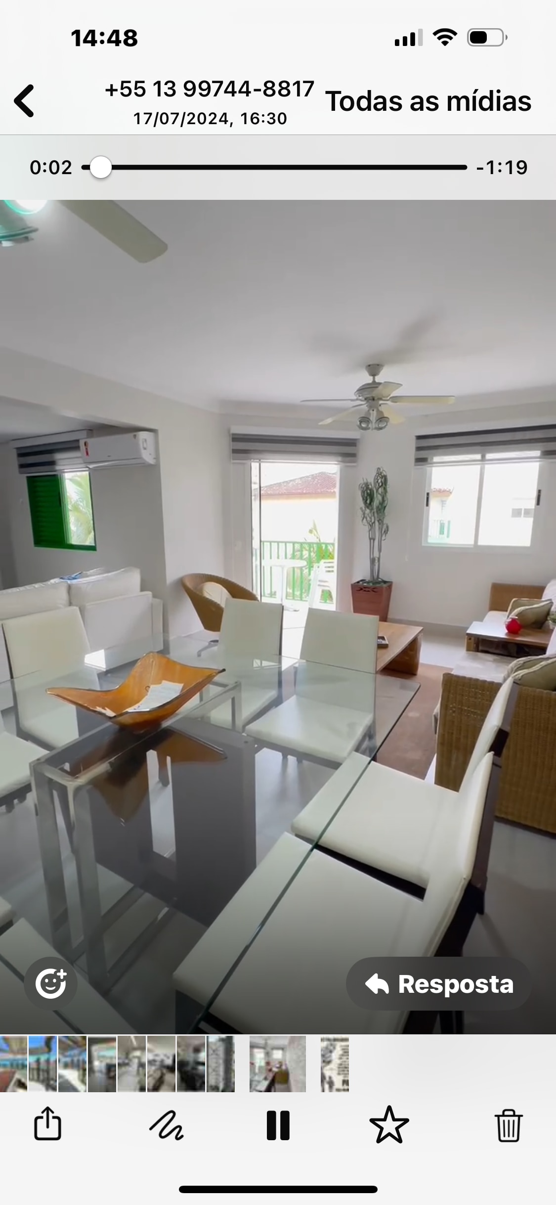 A bright dining area features a modern glass table surrounded by white chairs. Natural light enters through two large windows with light grey shades. A potted plant adds a touch of greenery, while a cozy seating arrangement creates an inviting space for relaxation.