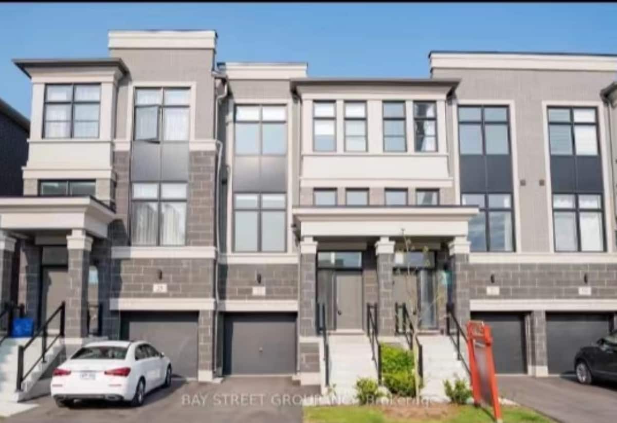 A modern multi-story building is shown, featuring a well-maintained facade with large windows. Two sets of steps lead to the main entrance, flanked by neatly trimmed grass and landscaping. A white vehicle is parked in front of the garage, completing the inviting exterior.