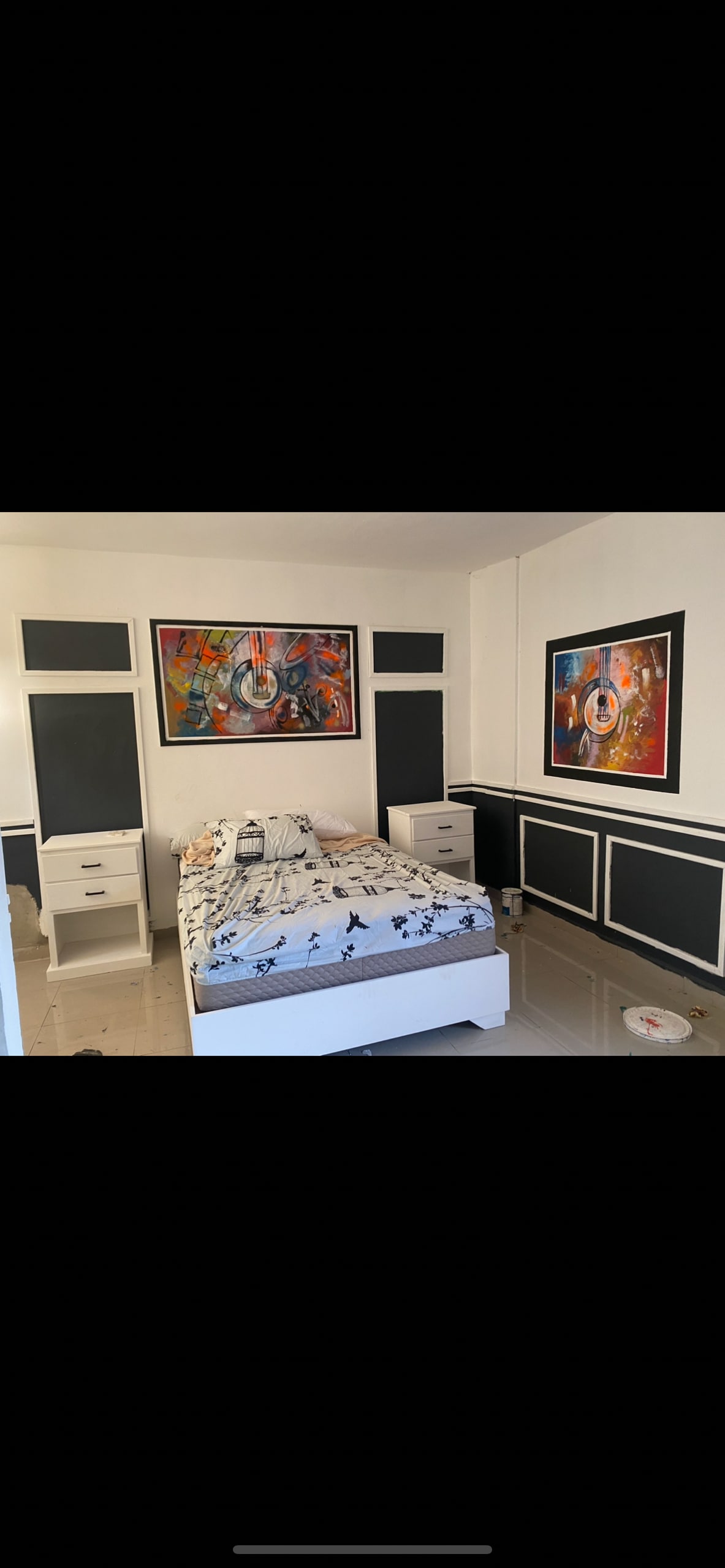 A contemporary bedroom is featured, with a light-colored bedspread adorned with a floral pattern. Abstract artwork hangs on the walls, adding pops of color. Two nightstands with drawers flank the bed, and a sleek desk is positioned against one wall.