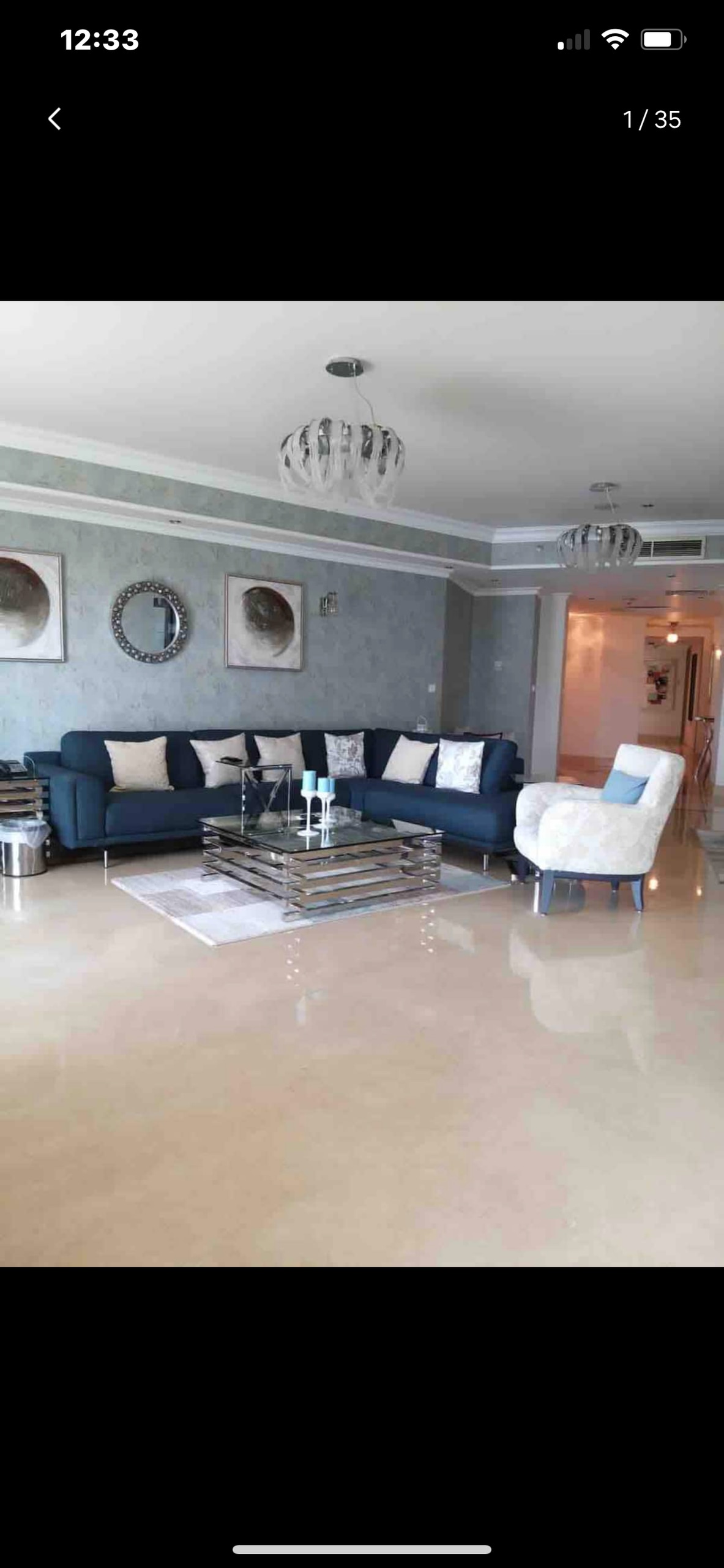 A light-filled living area features a navy blue sectional sofa adorned with decorative pillows. A glass coffee table rests on a neutral rug, complemented by two modern lighting fixtures overhead. Artwork is displayed on the walls, enhancing the contemporary design.