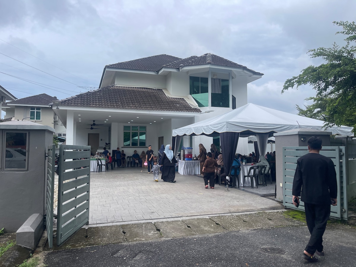 The exterior view showcases a spacious two-story house with a modern design and a large, covered outdoor area. A gathering of people is seen under a marquee tent, with tables set for an event. The driveway is paved and leads to the entrance.