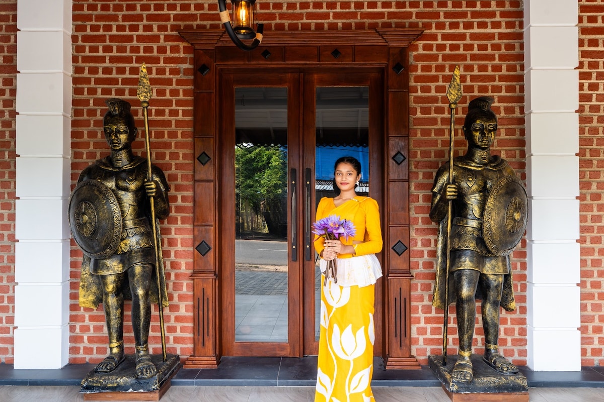 Two decorative bronze statues of armored warriors stand guard on either side of a double wooden door. A person dressed in a vibrant yellow outfit holds a bouquet of flowers, framed by a brick facade that adds character to the entrance.