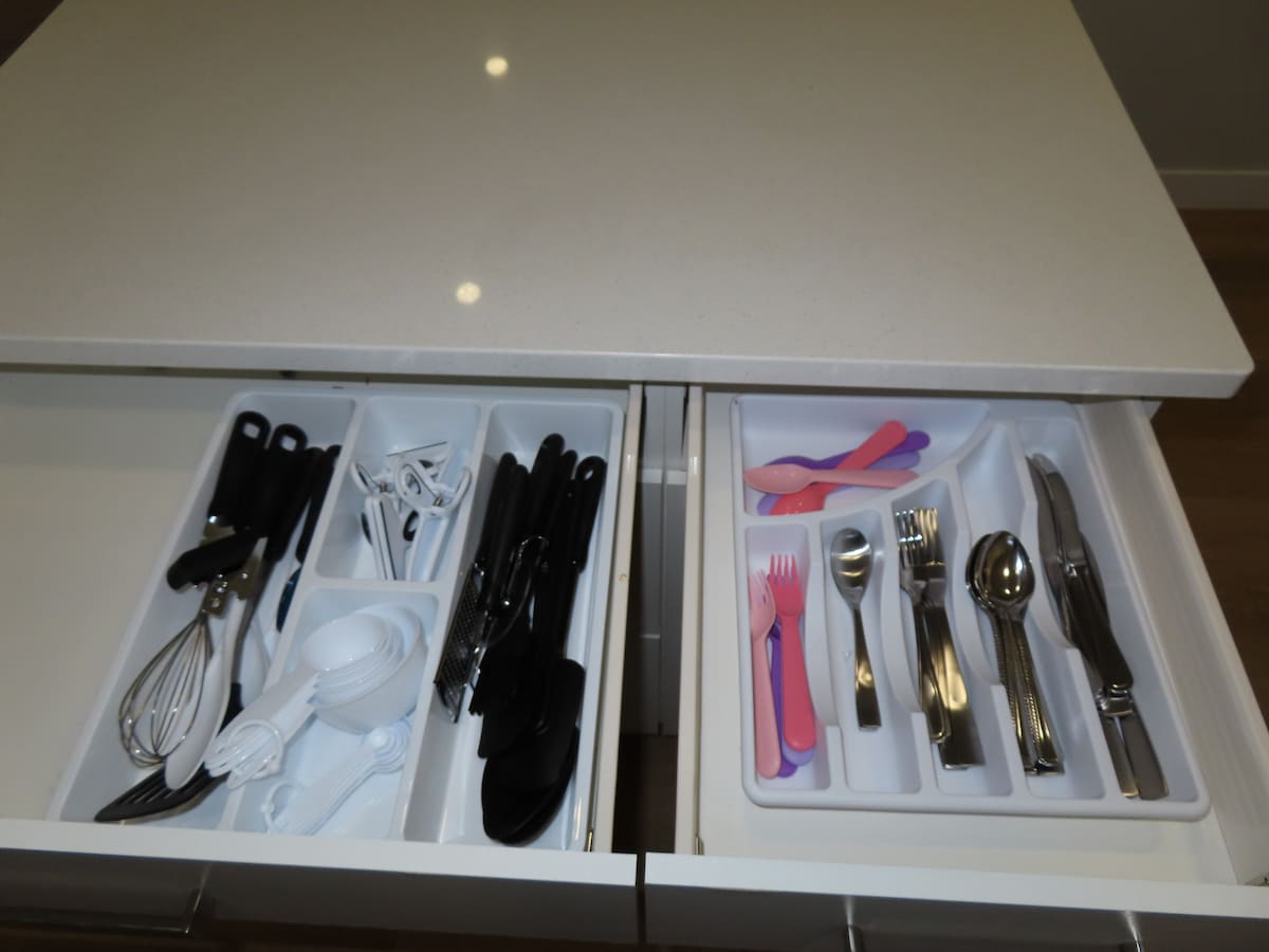 Kitchen drawers are shown, featuring organized utensils and tools. The left drawer contains various black and white utensils, including scissors and a whisk, while the right drawer showcases an assortment of silverware, including forks, spoons, and knives, all neatly arranged.