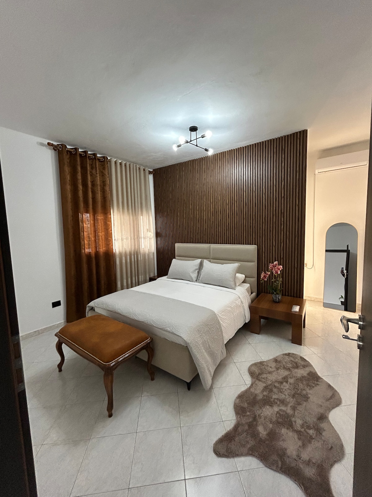 غرفة النوم 1 في فيلا كورتي هي ملاذ مضاء بأشعة الشمس على طراز البوتيك مع سرير فخم وستائر تعتيم وإضاءة دافئة بجانب السرير وخزانة ملابس مع شماعات واسعة - مثالية بعد يوم من الاستكشاف