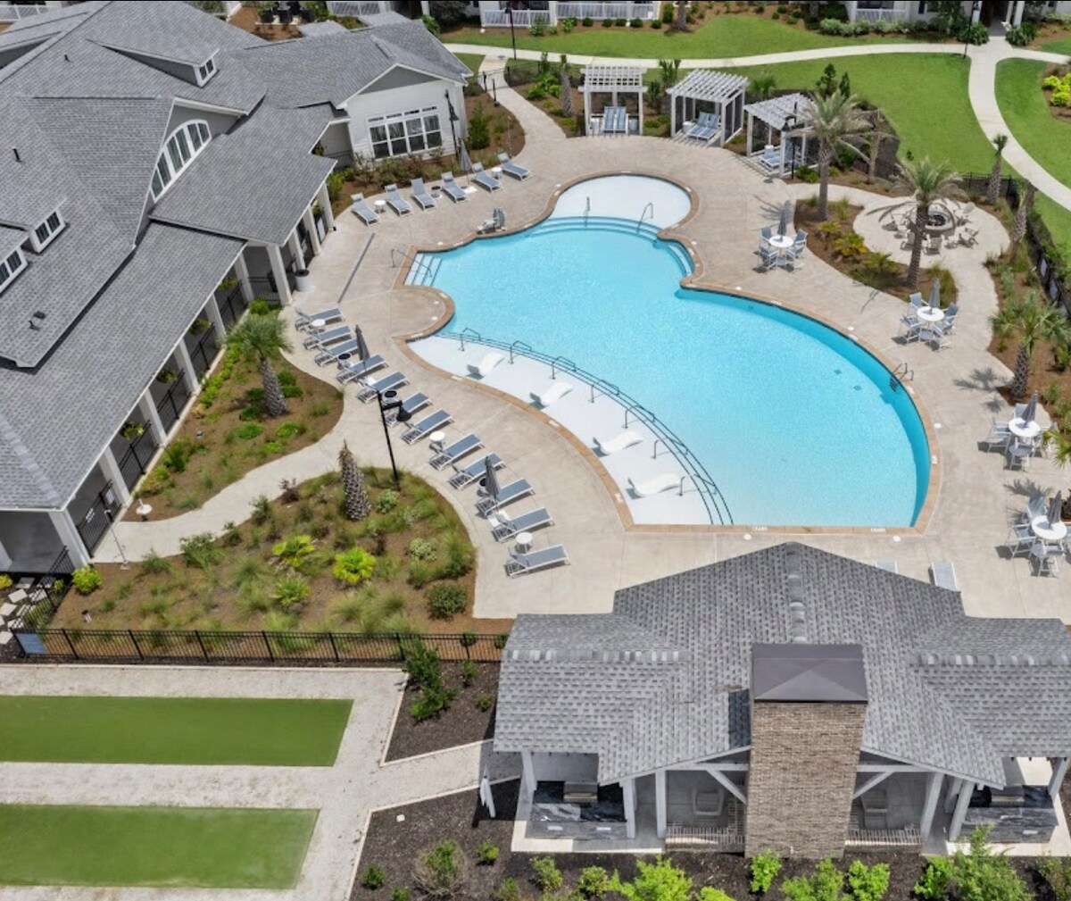 An expansive pool area is featured, showcasing a uniquely shaped swimming pool surrounded by lounge chairs and elegant cabanas. Lush landscaping, including palm trees and manicured greenery, enhances the outdoor recreational space, creating an inviting ambiance for guests to relax and unwind.