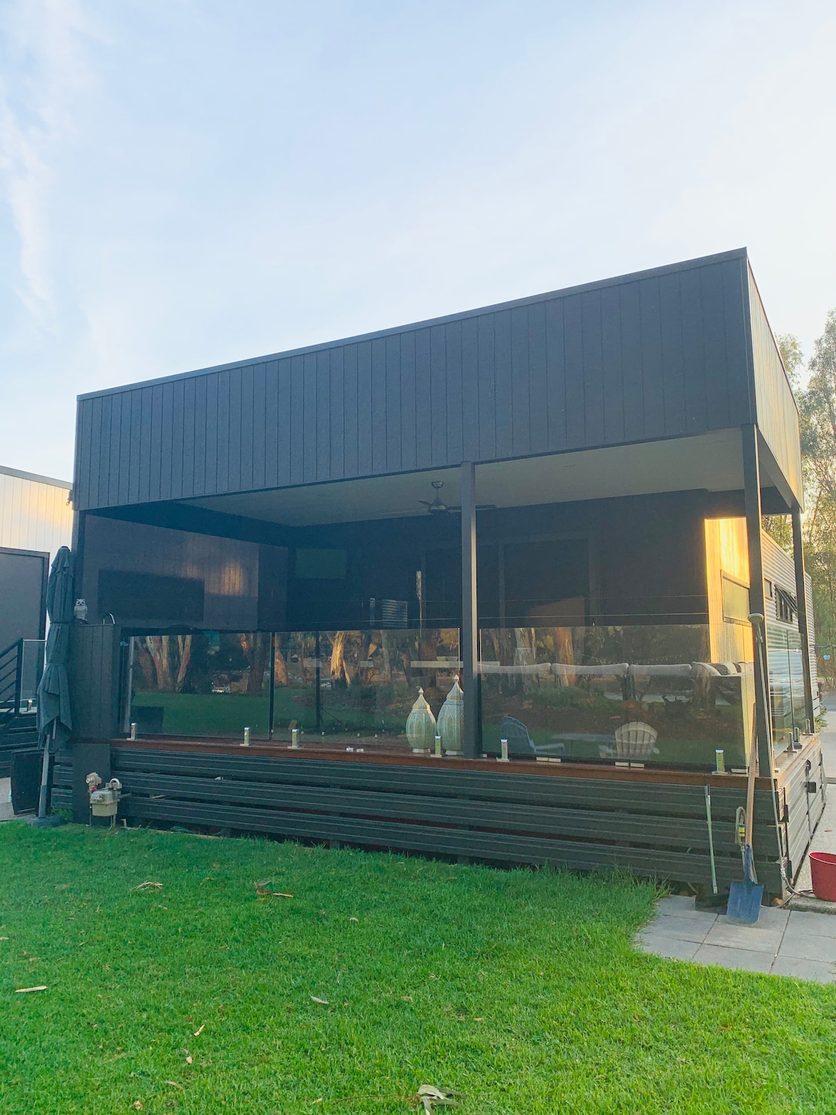 A modern exterior of a two-story structure is showcased, featuring a large deck with glass panels for unobstructed views. A well-maintained lawn surrounds the deck, enhancing the inviting outdoor space.
