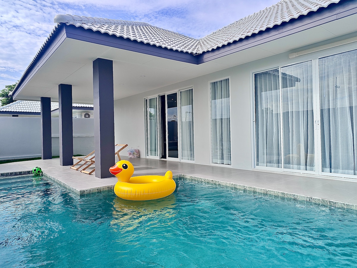 A private pool area is featured, with a bright yellow inflatable duck floating on the water. The smooth, tiled surface surrounds the pool, and large glass doors lead into the villa, enhancing the connection between indoor and outdoor spaces.