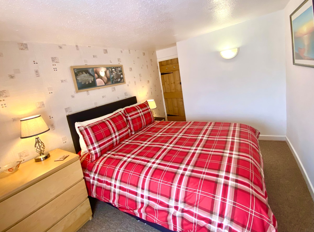 Galloway Cottage main bedroom with a set of drawers, bedside table & a built in wardrobe with full length mirror.  The bedside lamps have USB charging points.