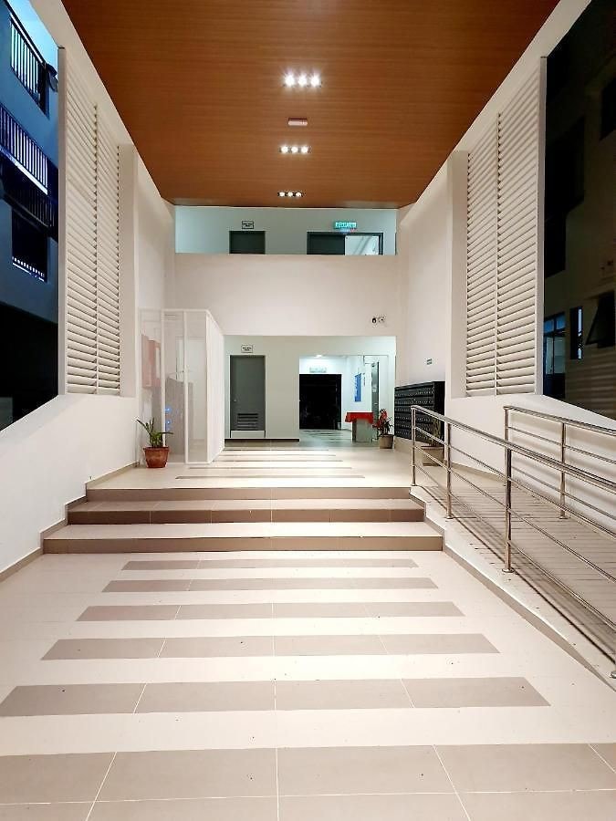A spacious entrance area is depicted, featuring a series of wide, textured steps leading up to a higher level. Light-colored walls are complemented by a dark wood ceiling, while potted plants are positioned beside transparent glass doors. Well-placed illumination highlights the clean architectural lines.