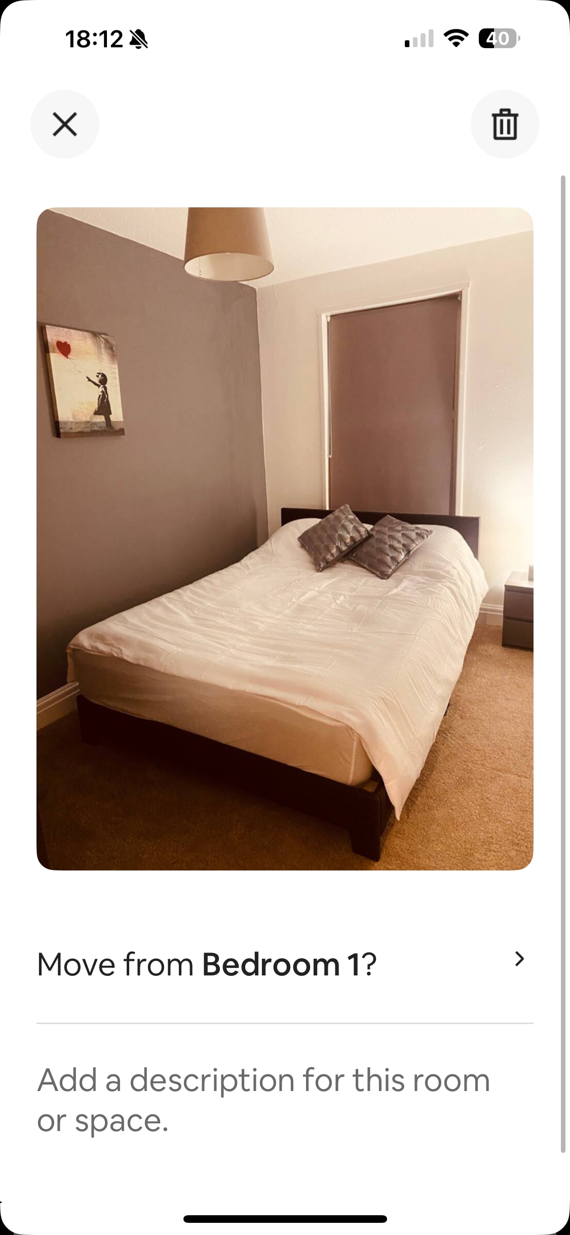 A bright bedroom features a spacious bed dressed in neutral bedding. Two pillows rest against the headboard. A bedside table sits on either side, with one lamp providing soft illumination. A window with a closed blind allows for privacy while maintaining a cozy atmosphere.