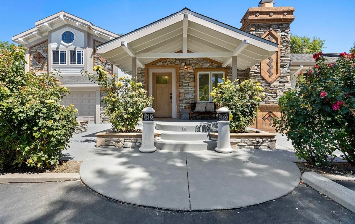 The exterior showcases a charming entrance with a stone façade and a covered porch. Two elegant columns frame the steps leading to the door, while blooming shrubs add natural beauty to the welcoming facade.
