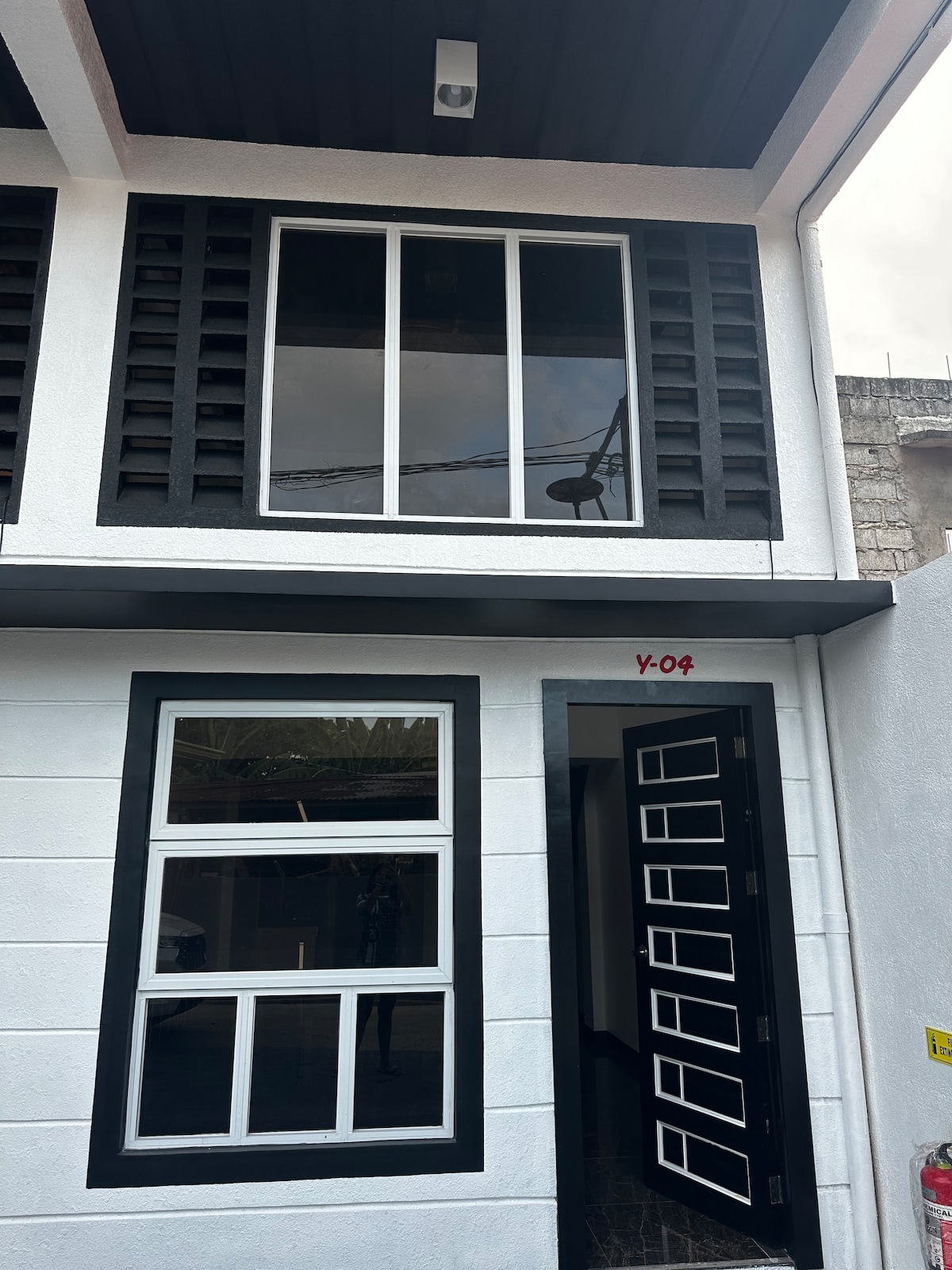 The exterior of the building features modern black and white design elements. Large windows provide natural light, while a sleek front door with a geometric pattern enhances the entrance. A dark awning above protects the doorway from the elements.