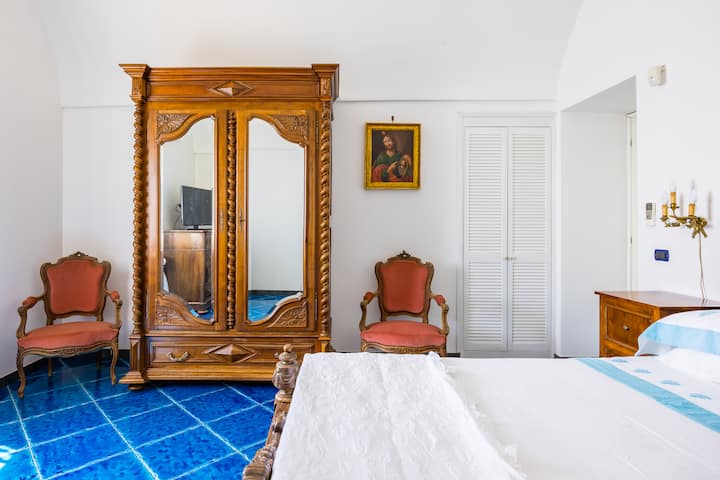 غرفة نوم مزدوجة مع مرتبة بحجم كينج، وغطاء من الريش، وخزانة ملابس خشبية، وطاولات بجانب السرير، وخزانة، وكرسيين بذراعين يطلان على البحر