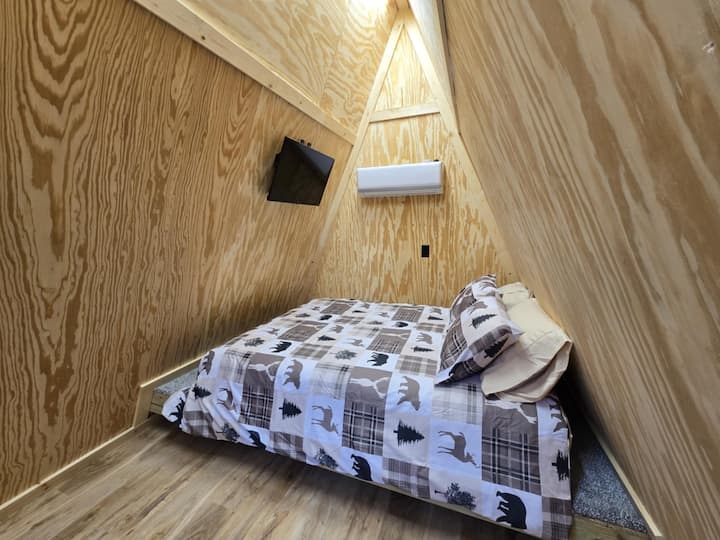 This snug A-frame bedroom offers a rustic yet modern retreat, with its warm wooden walls and charming wildlife-themed bedding. Perfectly cozy for winding down after a day of exploring, it’s an inviting space to relax and recharge.