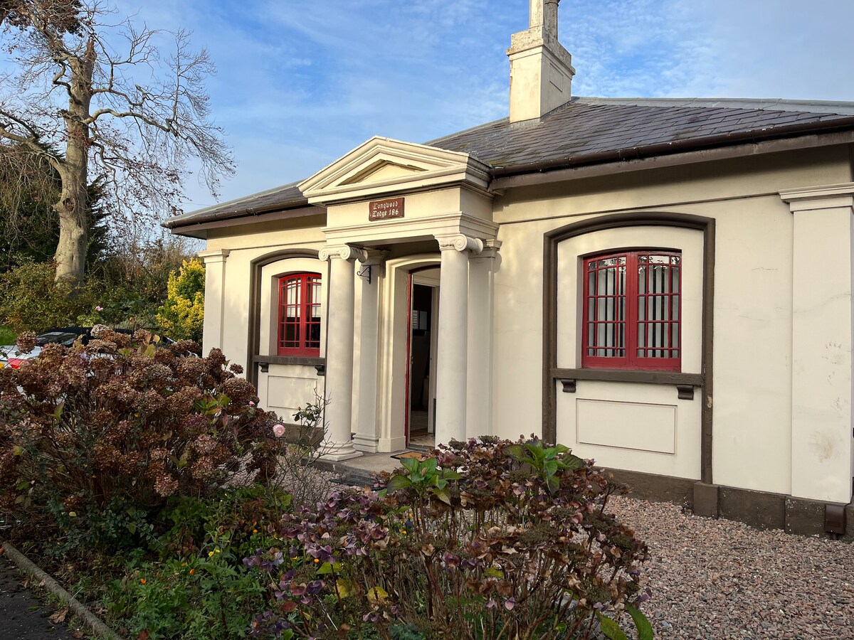 The exterior of a charming listed building features distinctive architectural details, including a prominent entrance framed by red-framed windows. Surrounding flowerbeds with blooming plants add a touch of greenery to the well-maintained grounds, contributing to the inviting appearance of the property.