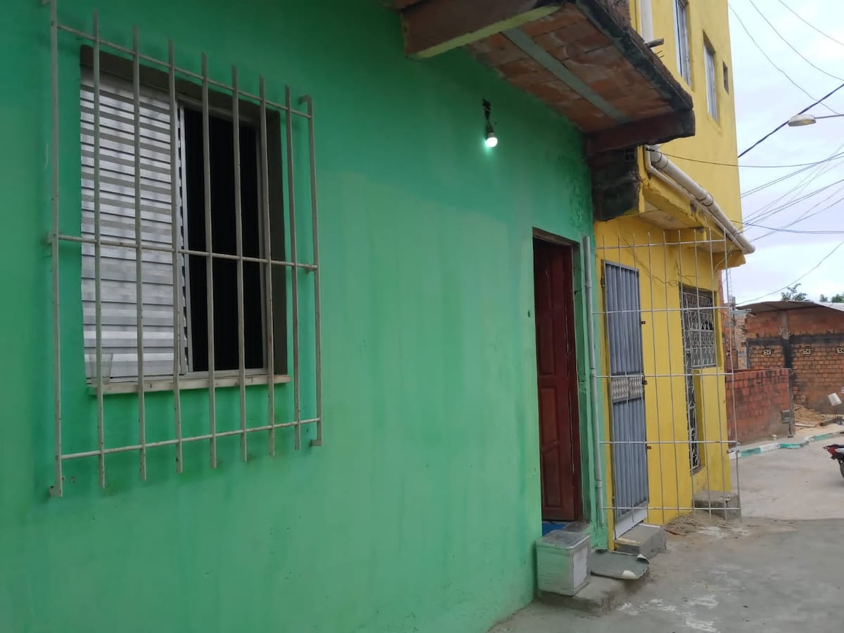 The exterior of a vibrant green building features a door framed in a deep red hue. A barred window allows natural light, enhancing visibility. Nearby, a yellow structure stands, contributing to the colorful atmosphere of the neighborhood.