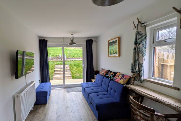 Chumba hiki kina baa ya kifungua kinywa ambayo ina wageni 4/5 pamoja na kitanda cha sofa na televisheni.  Milango inayoteleza inafunguka kwenye staha na bustani ya nyuma ambayo imewekwa kama  nyasi.  Nje kuna eneo la kula nje la meza ya pikiniki, sehemu ya kuchomea nyama na pia ufikiaji wa mashine ya kufulia.