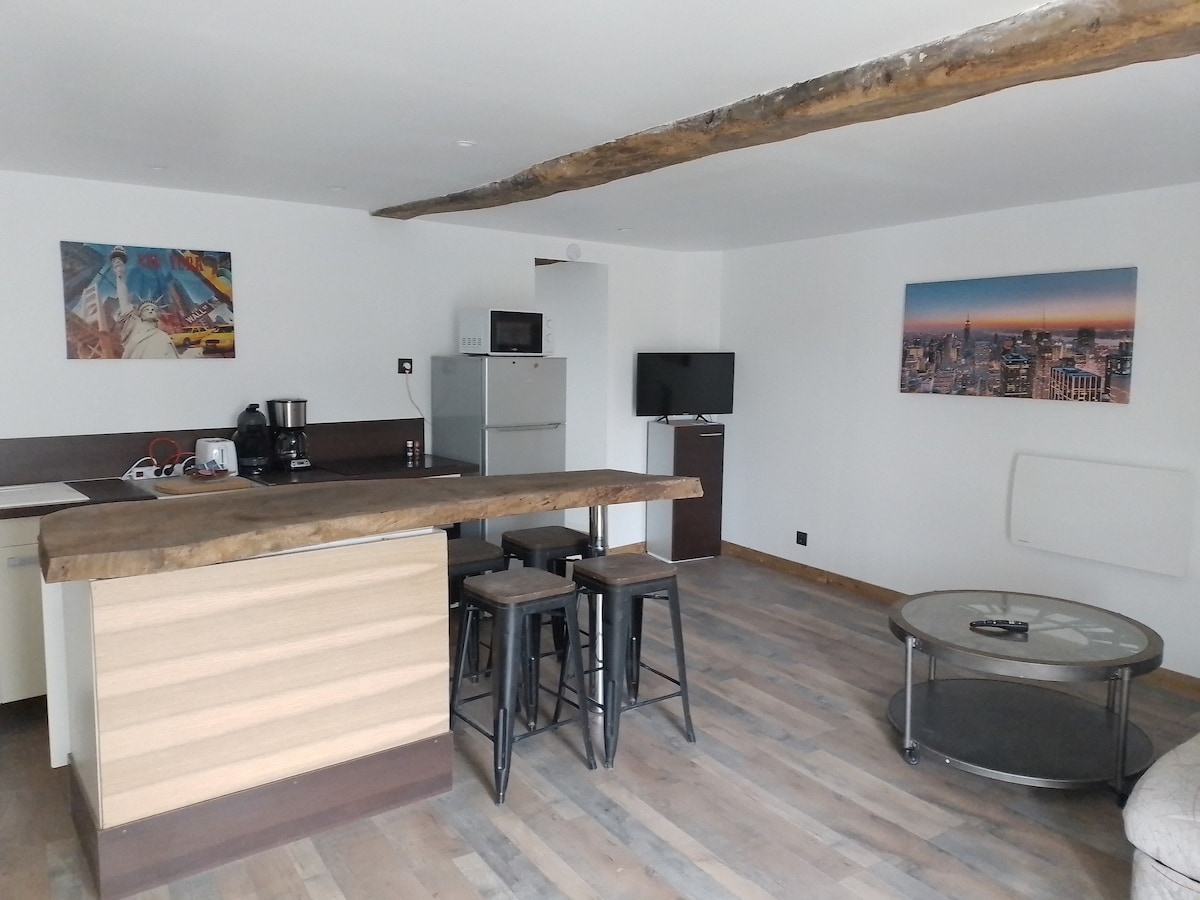 An open living space is depicted, showcasing a wooden breakfast bar with three stools. A contemporary kitchen area includes essential appliances. A circular coffee table is placed on the wooden floor, while art pieces adorn the walls. A television is mounted for entertainment.