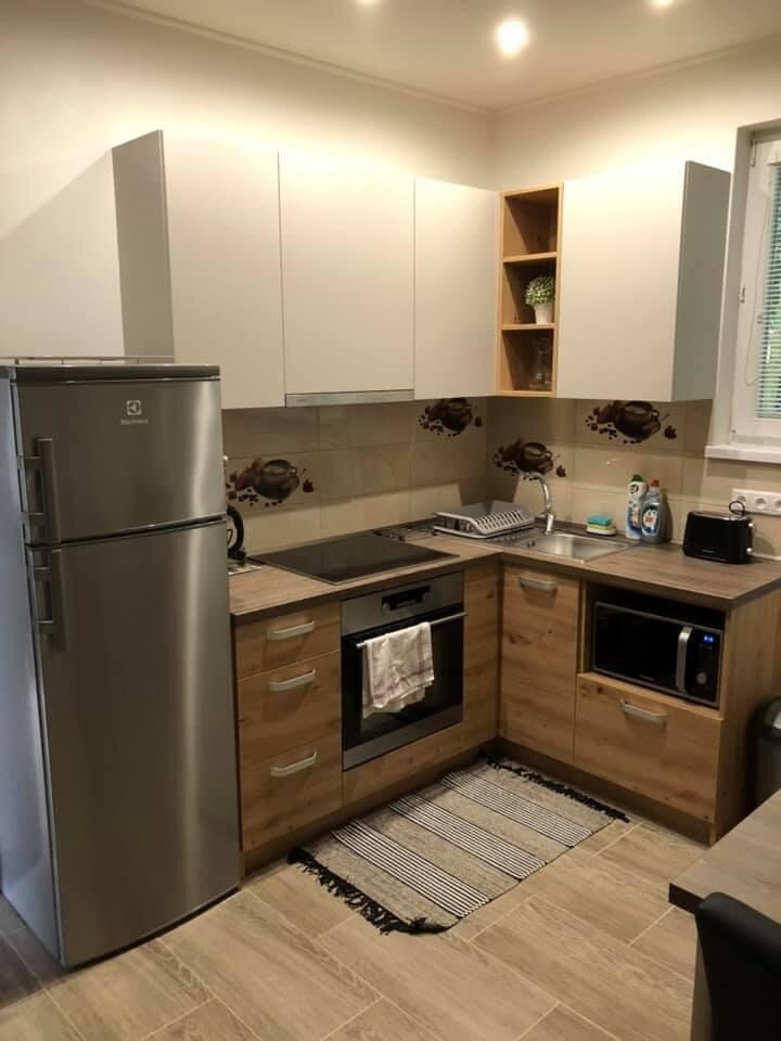 A functional kitchen features modern appliances, including a stainless steel refrigerator and an electric stove. Wooden cabinetry provides ample storage, complemented by a neatly arranged countertop with a dish rack and microwave. A subtle patterned rug lies on the tiled floor.