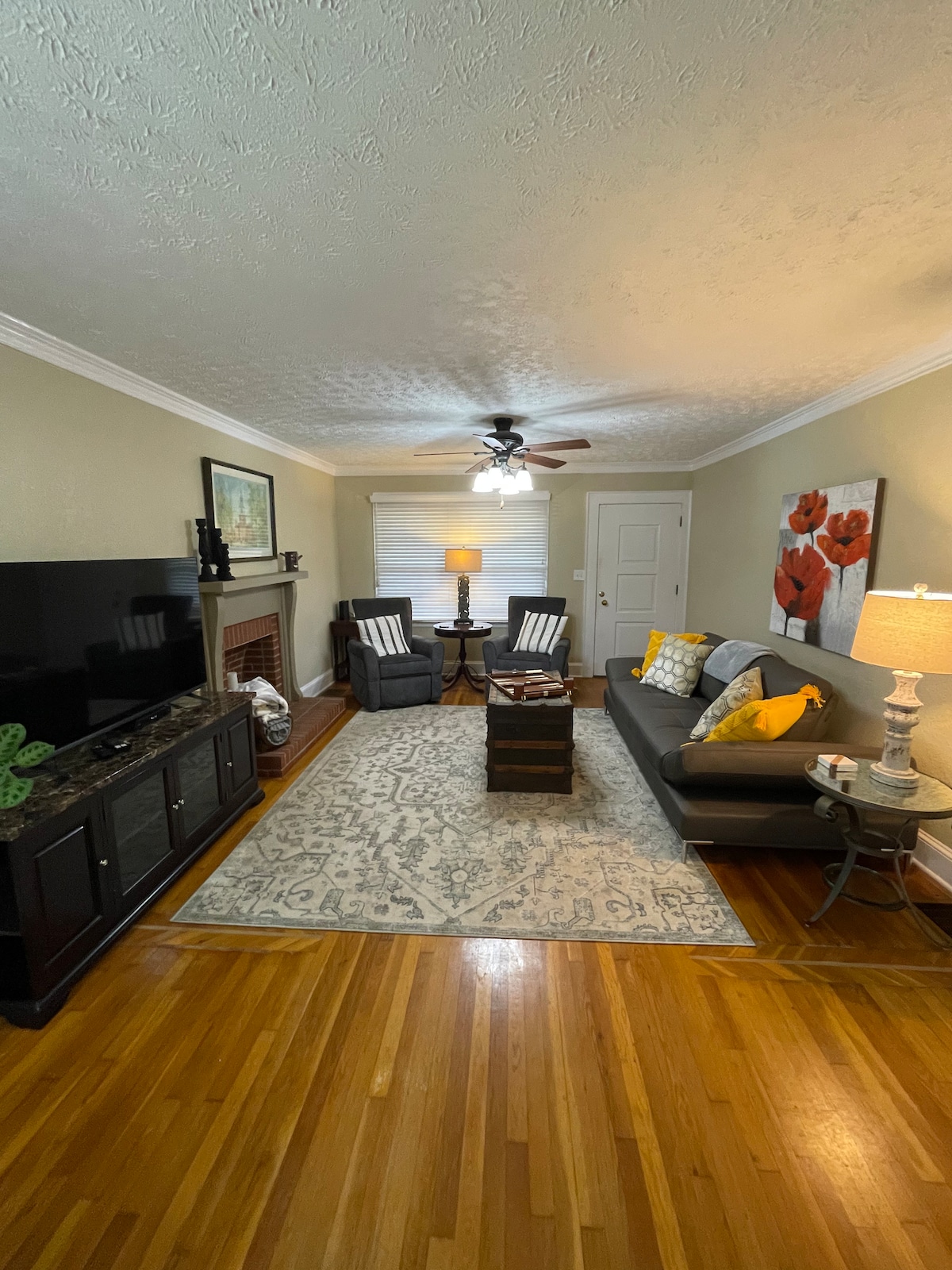 The living room features a comfortable sofa with decorative pillows, paired with two side tables and stylish lamps. A wall-mounted television is situated across from the seating area. A traditional area rug lays beneath a coffee table, enhancing the warm wooden floor.