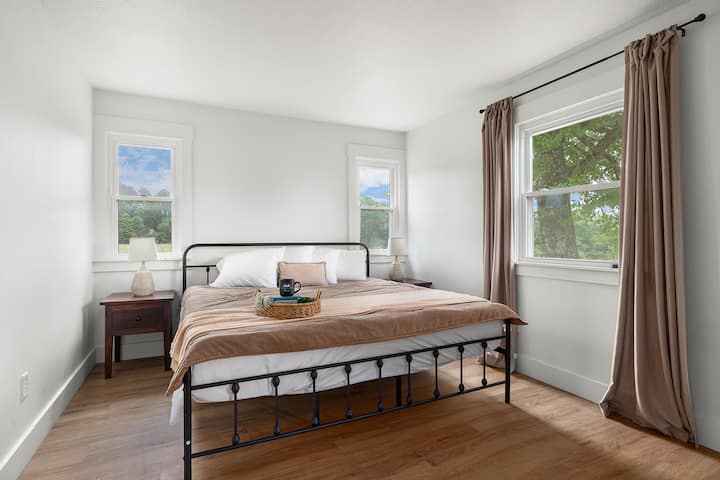 Primary bedroom with king bed, crisp white linens, warm wood accents, and soft natural light.