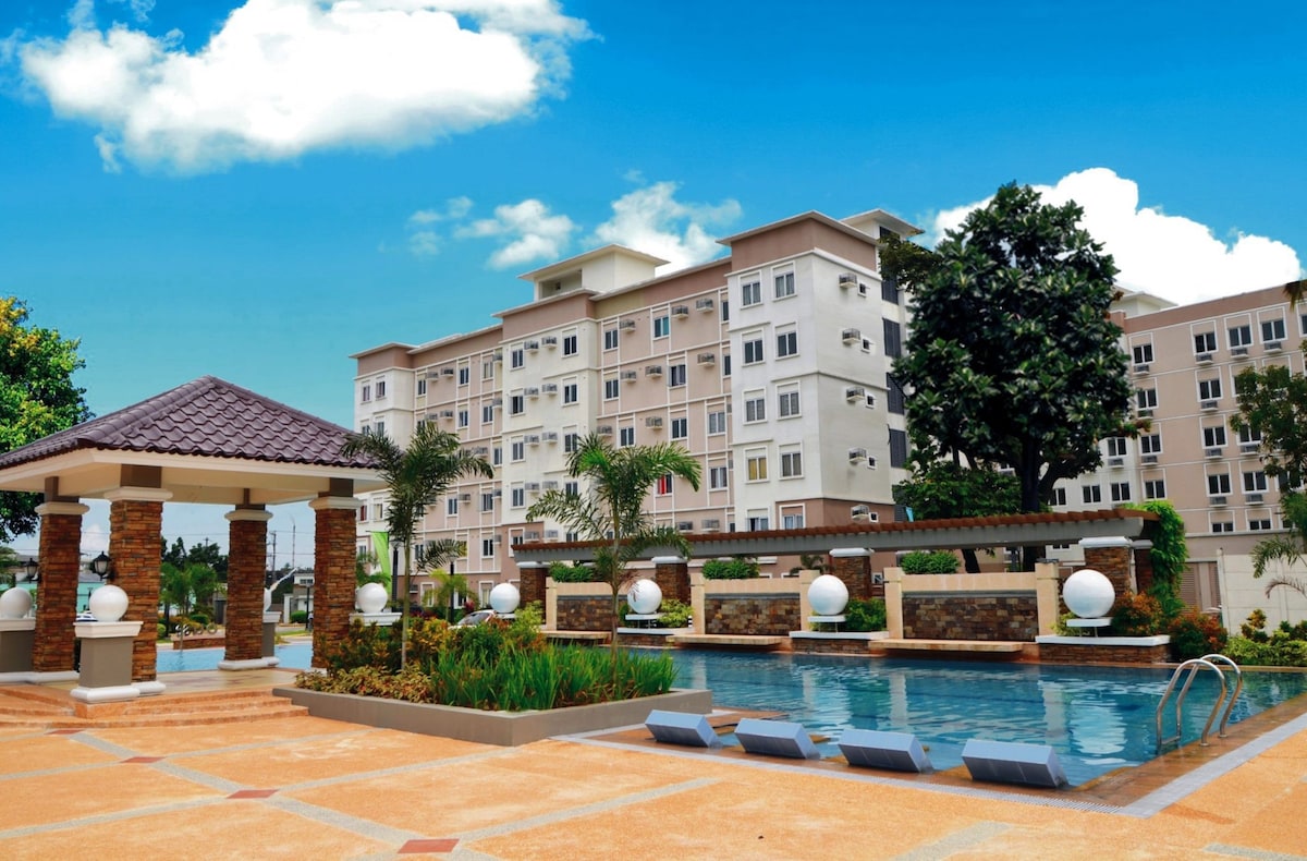 A spacious outdoor area features a crystal-clear swimming pool surrounded by well-maintained gardens. The building in the background includes multiple windows, providing natural light to the interior. Artistic light fixtures are placed strategically along the poolside, enhancing the inviting atmosphere.