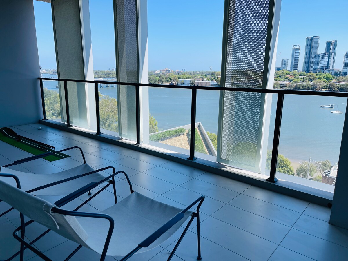 A spacious balcony features sleek lounge chairs and unobstructed views of the waterway. Large windows allow natural light to flood the area, showcasing the serene landscape beyond. The modern design enhances the open feel, creating a welcoming outdoor space for relaxation.