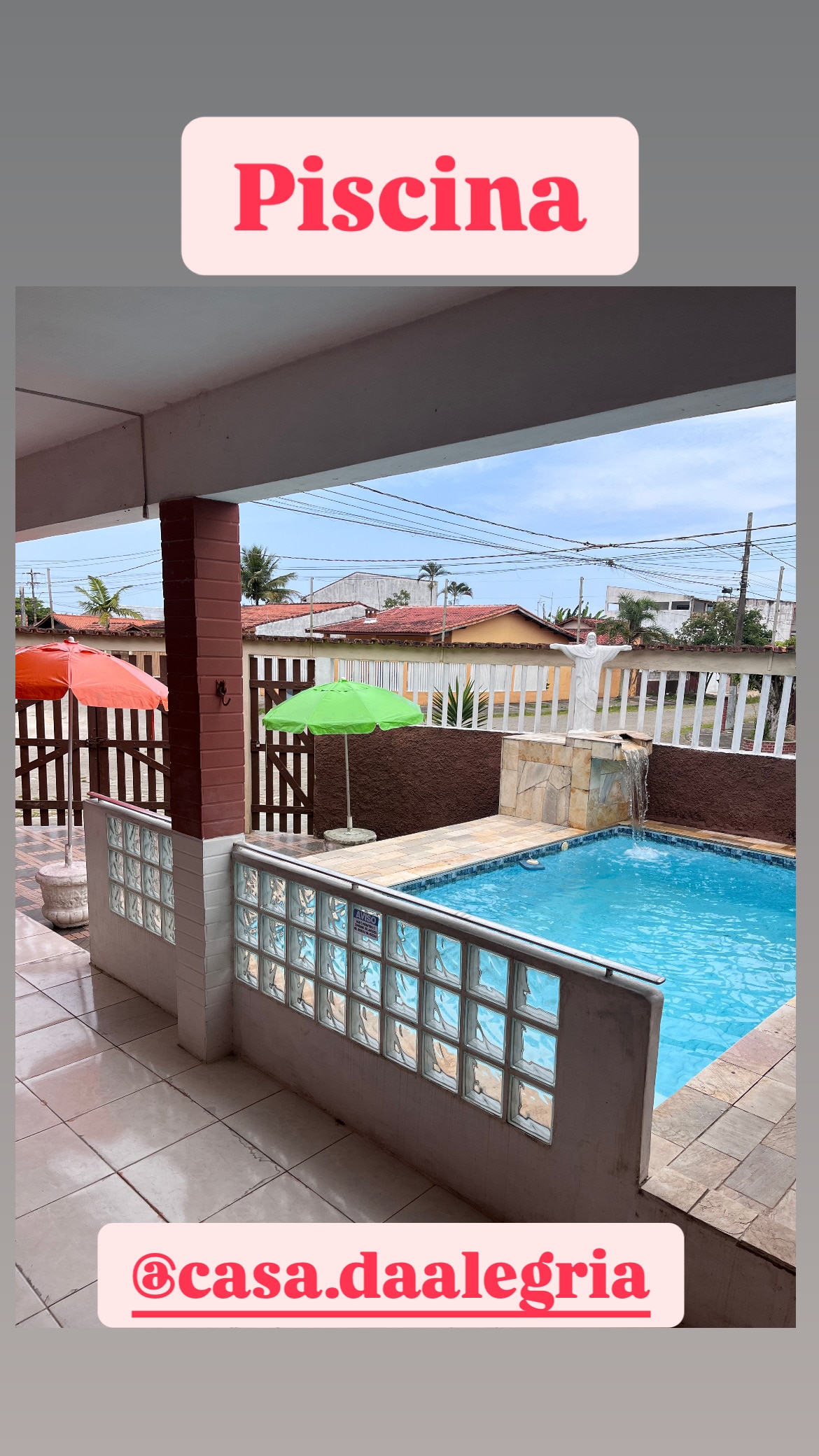 A private pool area is visible, featuring a rectangular pool with a gentle waterfall. Colorful umbrellas are placed adjacent to the pool on the tiled patio, providing shade. The surrounding area is enclosed with a decorative wall, enhancing the outdoor space.