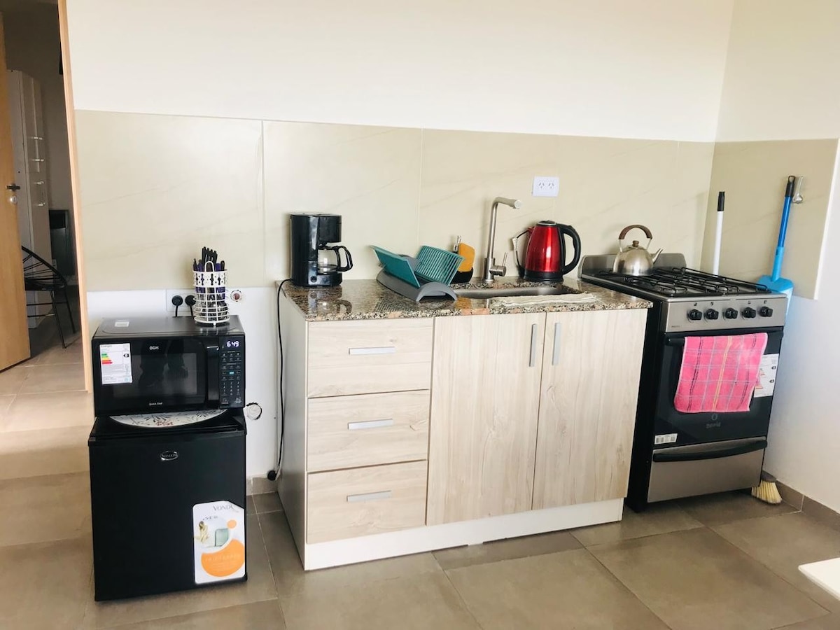 A fully equipped kitchen area features a range of appliances including a refrigerator, microwave, coffee maker, kettle, and stove. The granite countertops provide ample workspace, while neutral cabinetry offers storage. A sink is positioned centrally, contributing to the functionality of the space.
