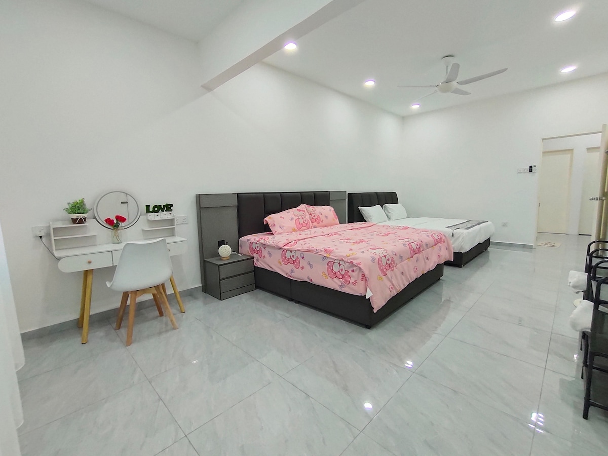 An airy room is showcased with two spacious beds, one covered in light pink bedding featuring playful designs. A simple desk and chair are positioned near a small decorative shelf. White walls and glossy tiles enhance the room's bright and clean appearance.