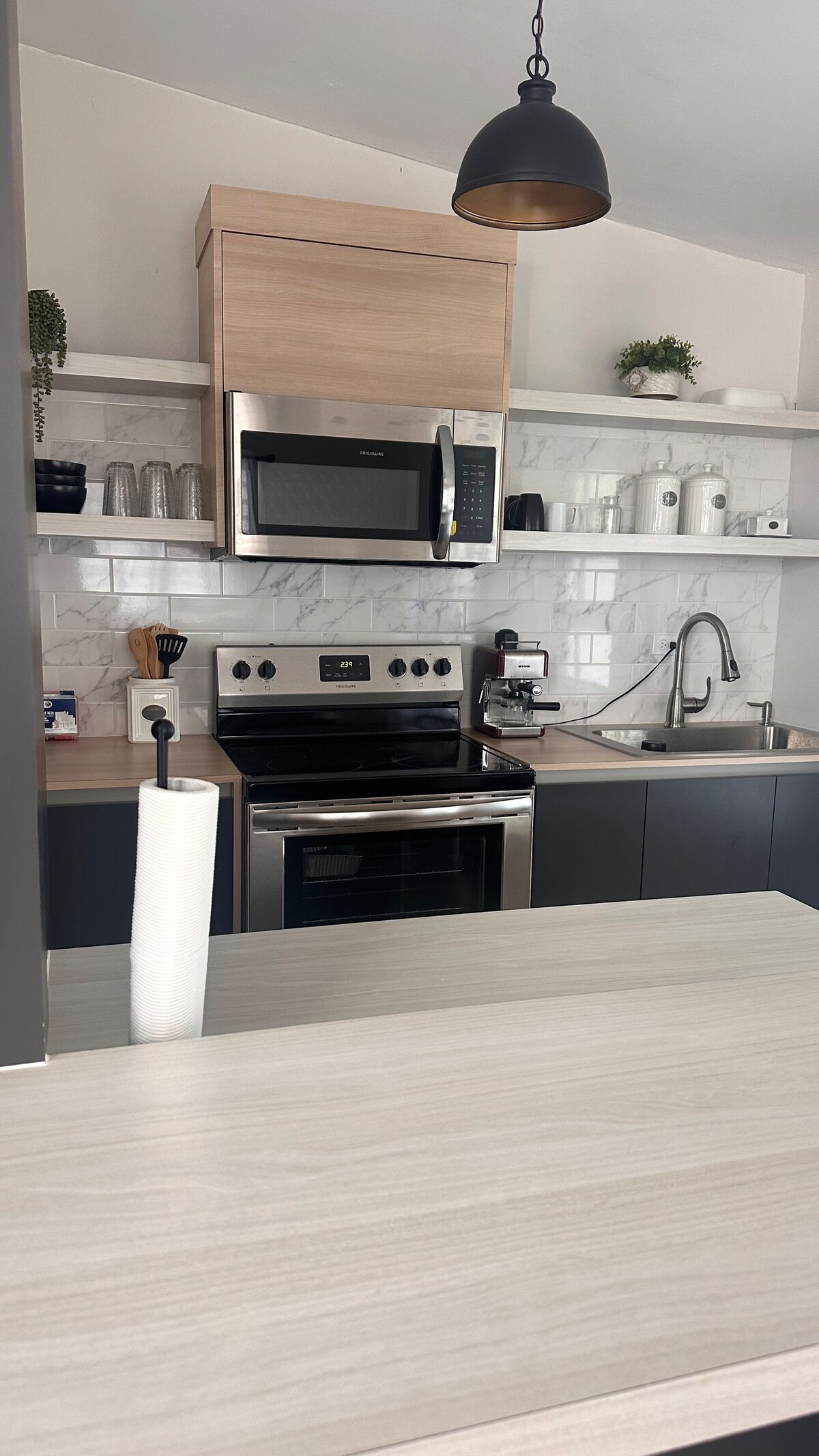 The kitchen features modern appliances, including a microwave and oven, set against light cabinetry and marble tile. Open shelving holds glassware and kitchen essentials, while a sleek countertop provides workspace and functionality.