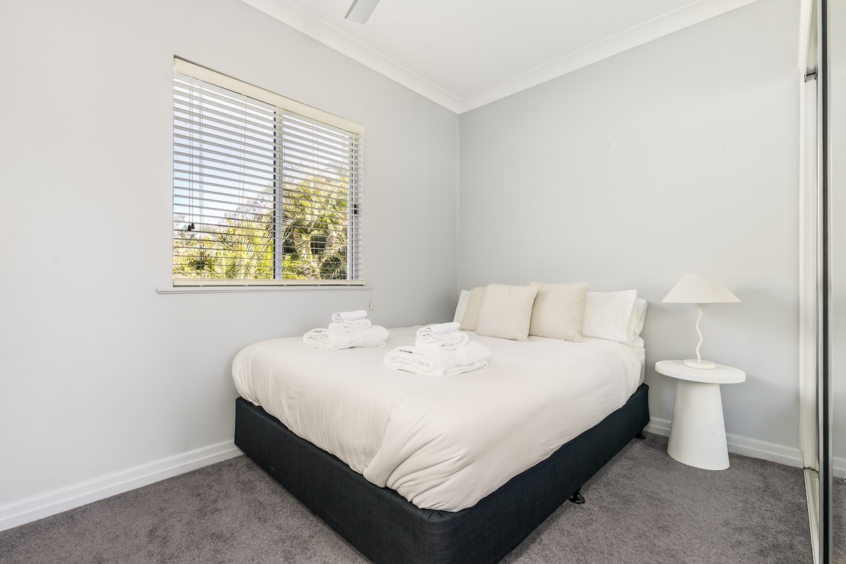 Dormitorio luminoso y acogedor con una cama tamaño queen y sábanas suaves. Esta habitación no tiene su propio aire acondicionado, pero 3 unidades de aire acondicionado en la casa mantienen baja la temperatura de los dormitorios y el ventilador de techo proporciona un flujo de aire adicional.