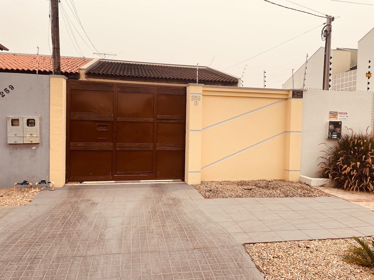 The exterior view showcases a secure entrance with a brown gate adjacent to a solid yellow wall. A paved pathway leads to the entrance, bordered by neatly arranged gravel and ornamental grass, suggesting a well-maintained outdoor space.