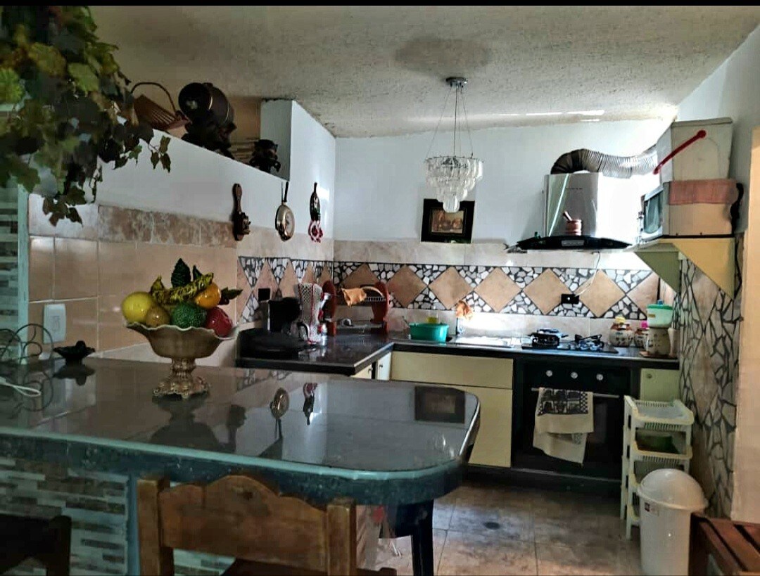 The kitchen is equipped with a blend of cabinetry and tiled walls, featuring a countertop with a fruit bowl. A stove and oven are positioned against one wall, while a chandelier provides overhead lighting.