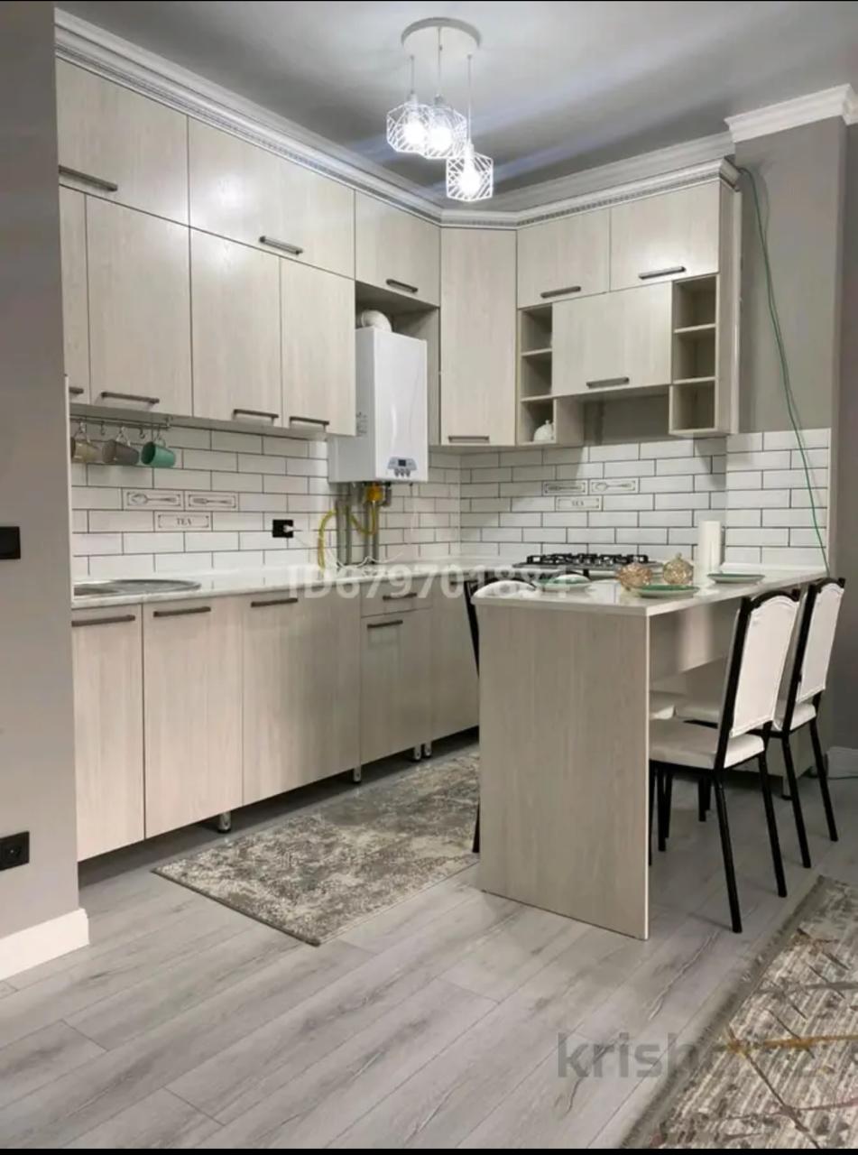 A modern kitchen is equipped with light wood cabinetry and a minimalist design. A compact dining area is integrated into the space, featuring a small table with two chairs. White tiles create a clean backsplash, and a rug adds warmth to the floor.