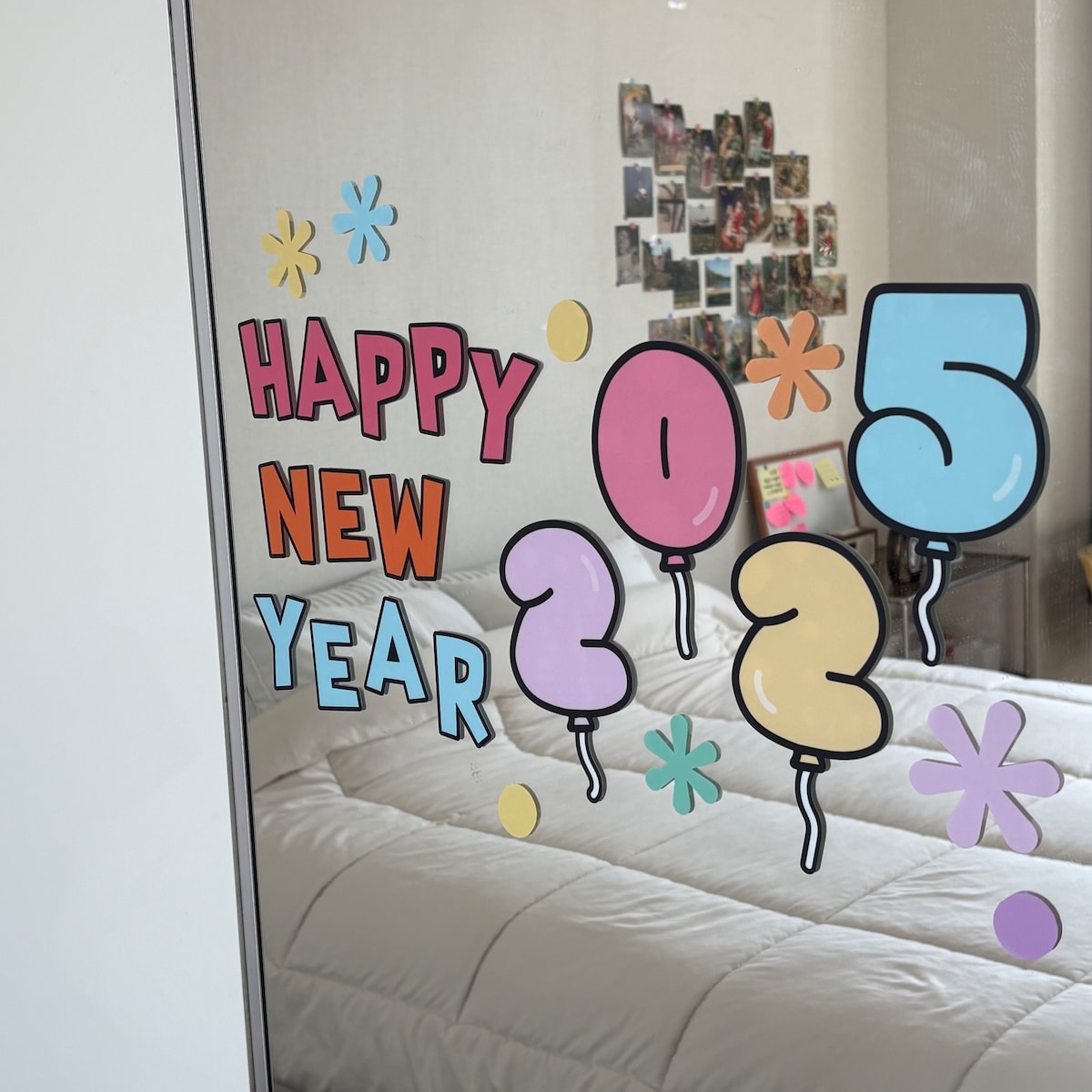 A glass panel displays festive decor celebrating New Year's with colorful balloons and text reading 'Happy New Year 2025.' Soft bedding is visible in the background, contributing to a cozy, cheerful ambiance.
