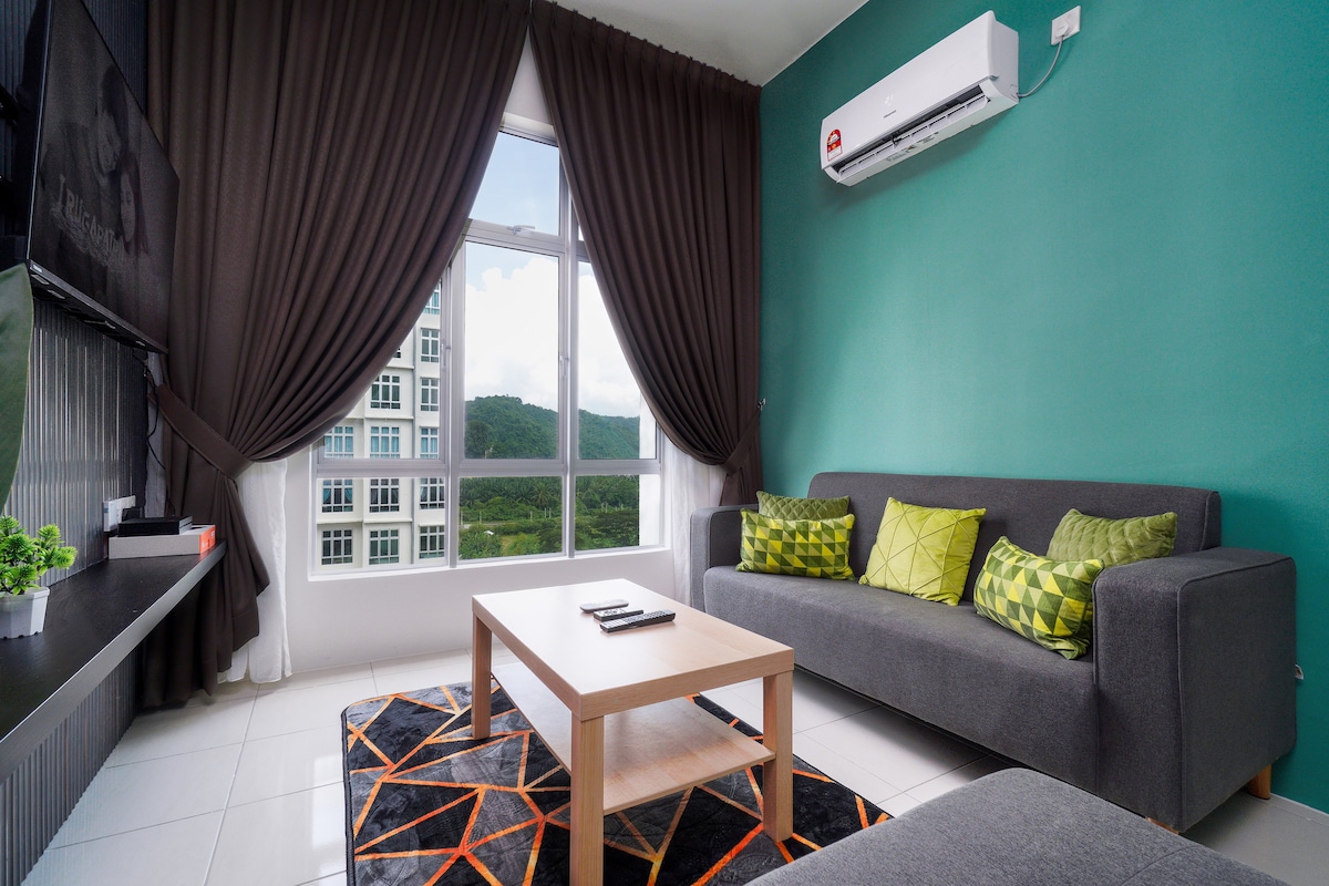 A contemporary living area features a gray sofa adorned with green cushions. A light wooden coffee table is placed on an orange and black geometric rug. Large windows provide views of the surrounding mountains, while dark curtains frame the bright space.