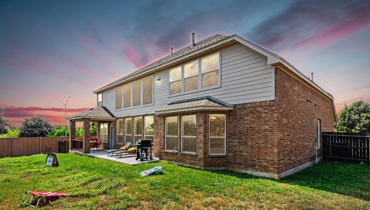 The two-story exterior of the home is framed by expansive windows, allowing natural light to illuminate the private backyard. A patio area is visible, featuring lounge chairs and a grill, while a grassy space offers ample room for outdoor activities.