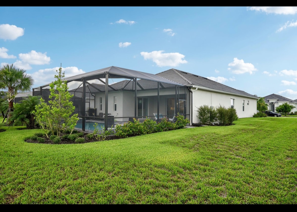 A large backyard is surrounded by well-maintained landscaping, featuring lush green grass and small trees. The screened patio covers a private pool area, providing a shaded space for relaxation. The home is positioned off to the side, allowing for open views of the serene environment.