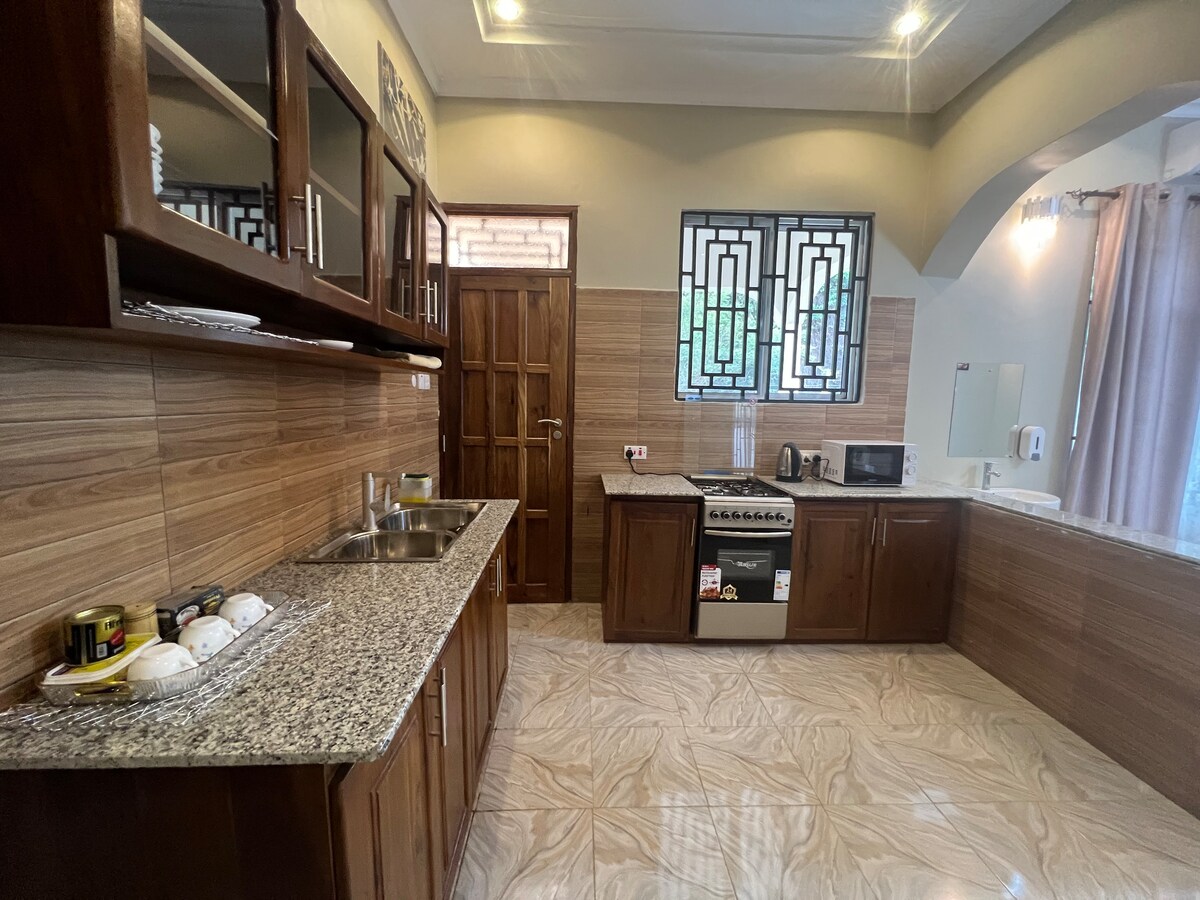 A well-equipped kitchen features wooden cabinetry and granite countertops. Stainless steel appliances, including an oven and microwave, are present. The space is illuminated by overhead lighting and natural light comes through a decorative window, enhancing the inviting and functional layout.