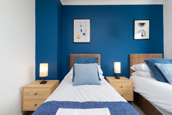Este vibrante dormitorio doble, con su llamativa pared de acento azul y lámparas individuales de noche, ofrece cómodos arreglos para dormir.