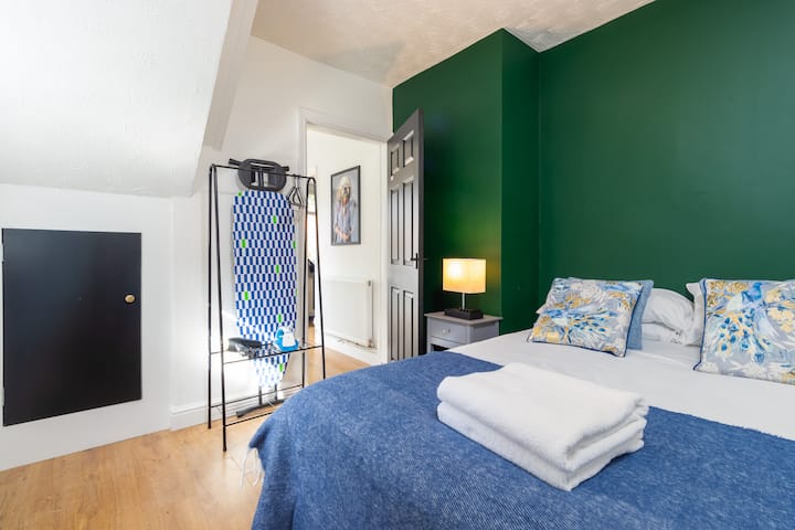 Este acogedor dormitorio cuenta con una cómoda cama con un tiro azul, una lámpara junto a la cama y una tabla de planchar para la comodidad de los huéspedes.